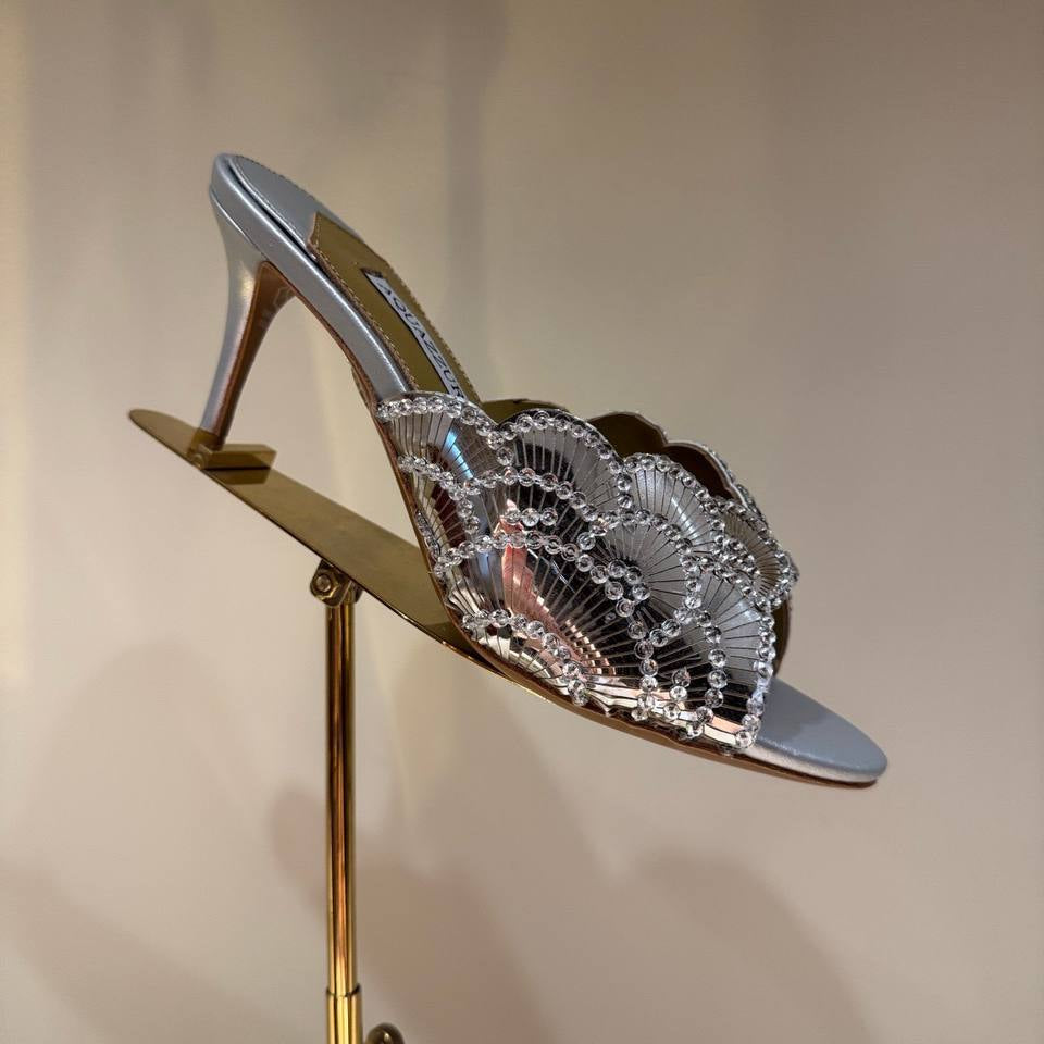 Pink high-heeled shoe with intricate design on a stand against a neutral background